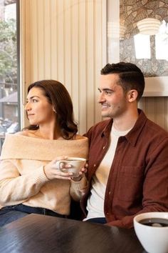 a man and woman sitting at a table with cups of coffee in front of them