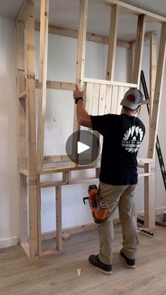 a man standing on top of a hard wood floor next to a wooden ladder and holding a saw