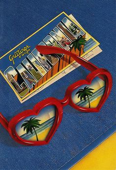 a pair of red heart shaped sunglasses sitting on top of a blue book next to a postcard