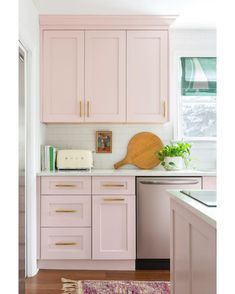 a kitchen with pink cabinets and wooden cutting board on the counter top next to a dishwasher