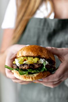 a person holding a hamburger in their hands with lettuce and cheese on it