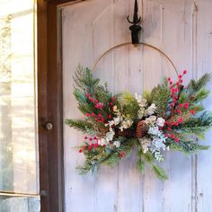 a wreath hanging on the side of a door with pine cones, berries and evergreens