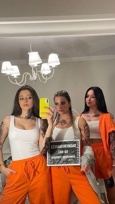 three women in orange pants are holding up a cell phone