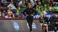 a woman standing on top of a basketball court with her hands on her hips as people watch from the sidelines