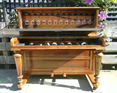 an old fashioned wooden box with wine glasses on the top and bottom, sitting in front of a fence