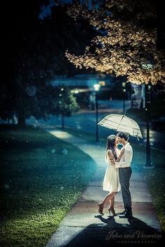 a man and woman kissing under an umbrella in the rain on a sidewalk at night