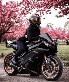 a person sitting on a black motorcycle in front of some trees with pink flowers behind them