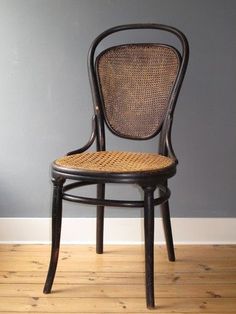 an antique chair with wicker seat and back rests against a gray wall in a room