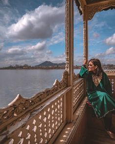 a woman is sitting on a balcony next to the water and looking out at the sky