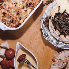 two dishes of food on a table with bread and other foods in bowls next to them