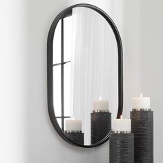 three candles are lit in front of a round mirror on the wall next to a window