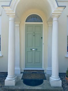 a green door with two pillars and a black mat on the front steps in front of a white house