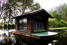 a small house sitting on top of a body of water next to a lush green forest