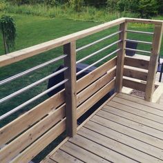 there is a wooden deck with metal railings on the grass field and trees in the background