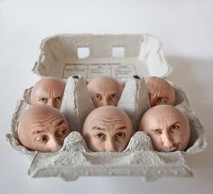 an egg carton with six bald heads in it and one man's face sticking out