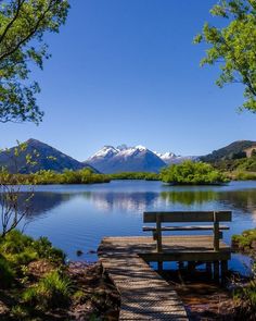 a bench sitting on top of a wooden pier next to a lake with mountains in the background