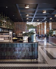 the interior of a restaurant with black and white tile flooring, potted plants on the bar