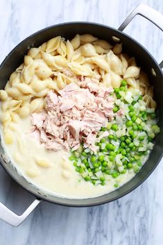 a pot filled with pasta and peas on top of a marble countertop next to a knife