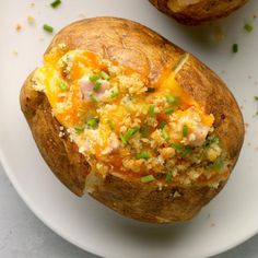 two baked potatoes on a white plate with green onions and cheese in the top half