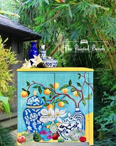 a cabinet painted with flowers and fruit on it in the middle of a garden area