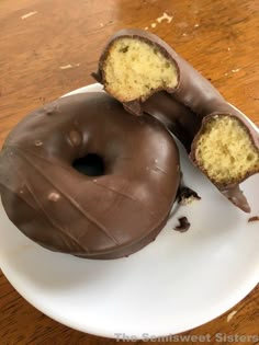 two chocolate covered doughnuts on a plate with one cut in half to show the inside