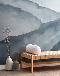 a wooden bench sitting in front of a wall with mountains painted on it and two vases next to it