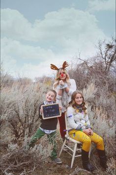 three children sitting on a chair in the middle of a field with an antelope head