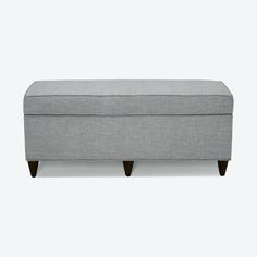 a gray bench with wooden legs and a cushion on the bottom, in front of a white background