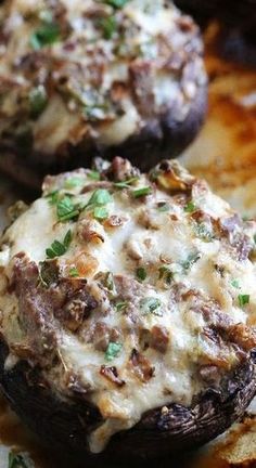 two stuffed mushrooms covered in cheese and parsley on top of a baking sheet with other food items