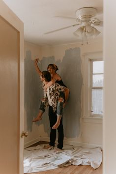 a man and woman standing on top of a wooden floor in a room with paint all over the walls