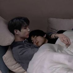 two people laying in bed with one person sleeping on the pillow and the other lying down