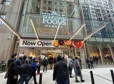 people are standing outside of a store in front of tall buildings with lights on them