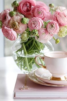 pink flowers are in a vase next to a cup and saucer