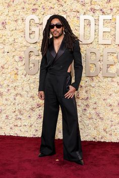 a man with dreadlocks standing on a red carpet wearing a black suit and sunglasses