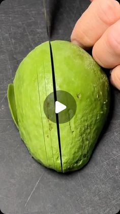 a person cutting an avocado with a knife on top of the green piece