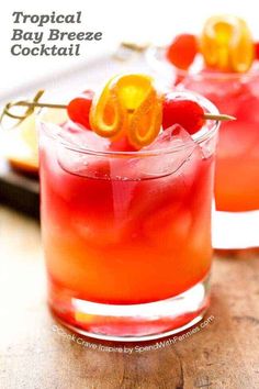 two glasses filled with red liquid and orange garnish on the rim, sitting on a wooden table