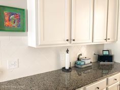 a kitchen with white cabinets and granite counter tops in front of a painting on the wall