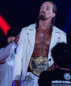 a man with long hair wearing a white jacket and gold belt standing in front of a crowd