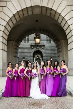 a group of women standing next to each other in front of a stone building holding bouquets