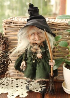 an old wizard doll holding a broom and potted plant in front of a wicker basket