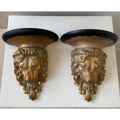 two golden lion head wall sconces on a white surface