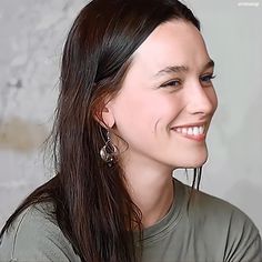 a woman with long hair smiling and wearing earrings on her head, in front of a white wall