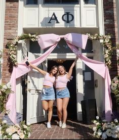 two young women standing in front of a building with pink sashes on the doors