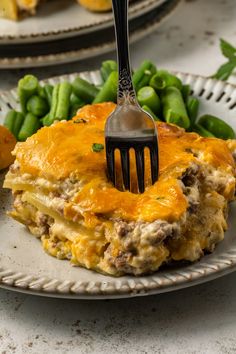 a fork is stuck into a piece of lasagna on a plate with green beans