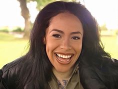 a woman with long black hair smiling and wearing a leather jacket over her shoulders,