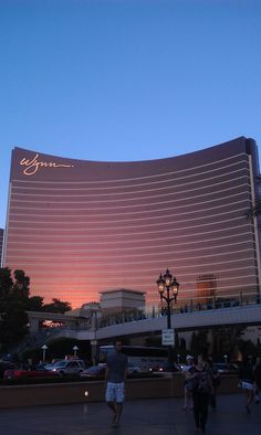 people walking in front of the las vegas hotel and casino at dusk, with lights on