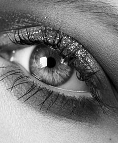 a woman's eye with long lashes and blue eyeshade, black and white photo