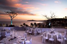 an outdoor dining area with tables and chairs set up for dinner overlooking the ocean at sunset