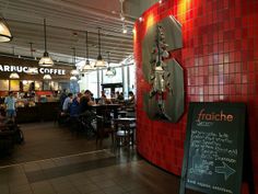 people sitting at tables in a restaurant with red tiles on the wall and signs hanging from the ceiling