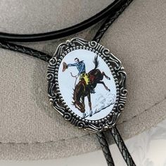 Our handmade western cowboy bolo tie has a vintage rodeo cowboy with a glass coating. PERFECT for a country men’s bolo tie, wedding sting tie, necktie for groomsmen, or any special person in your life. This bolo tie for men (and women!) has a metal clamp which makes it easy to adjust.   *Makes a Great Gift*  Pendant Size: 1.5 in x 1.25 in  Cord in Black Genuine Leather: 39in Gold Bow Tie, Yellow Bow Tie, Purple Bow Tie, Green Bow Tie, Plaid Bow Tie, Rodeo Cowboy, Tie For Men, Pink Bow Tie, Bowtie And Suspenders